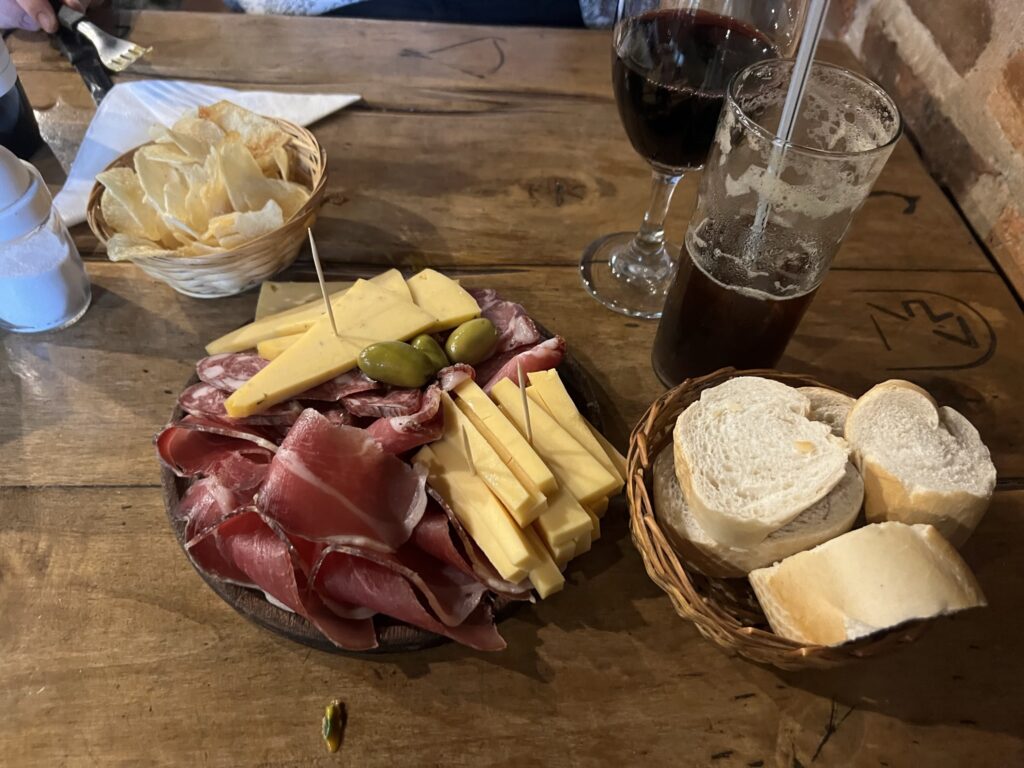 A plate of meat, bread and wine on a wooden table.