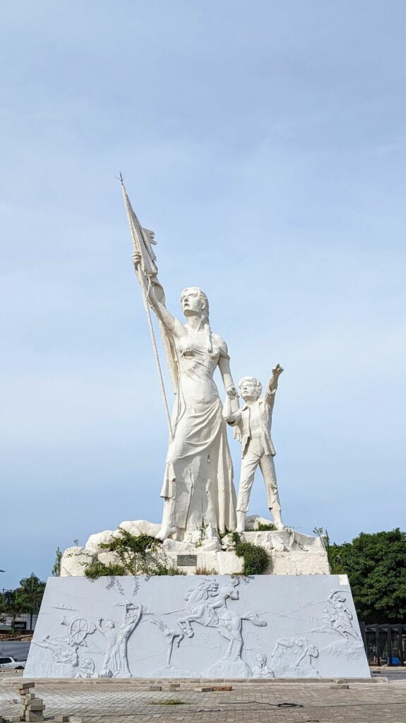 A white statue of a woman holding a torn flag and a child pointing to the sky