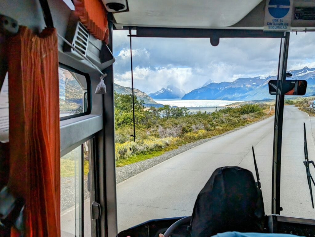 A cozy bus interior with passengers seated, looking out of the window at the passing scenery, including a glacier.