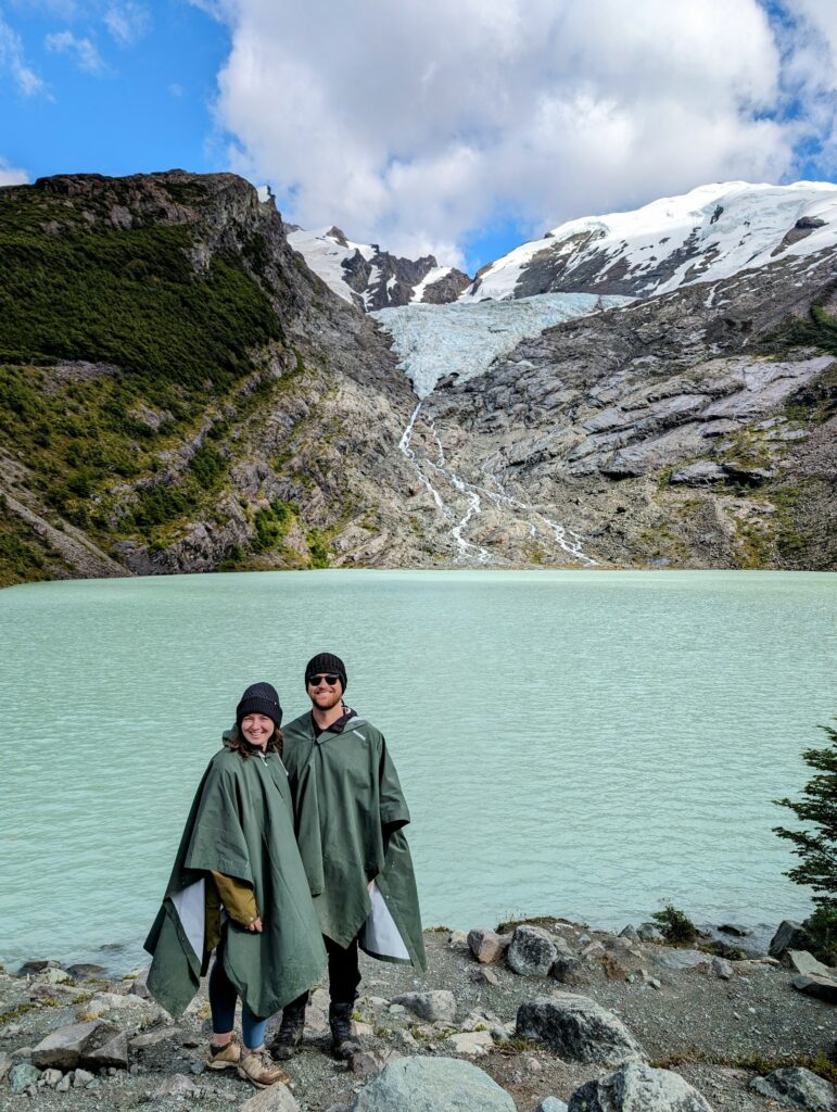 Two people standing in front of a teal lake with a glacier on the mountain