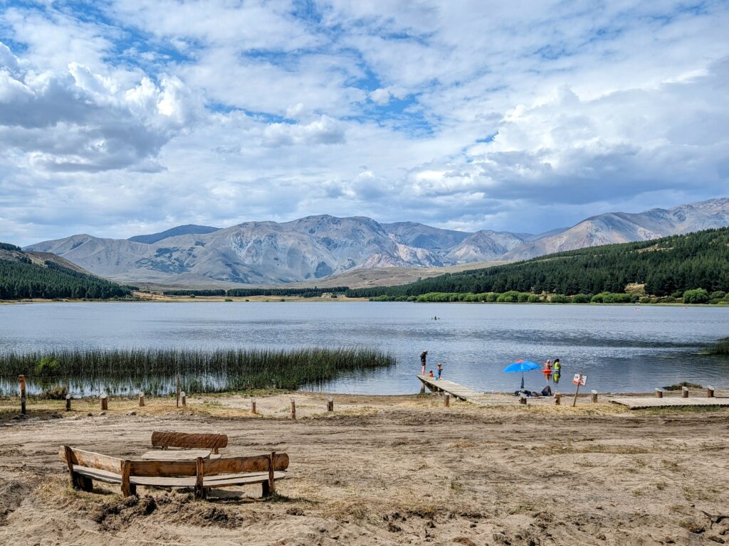 A beach in front of a mountain lake surrounded by