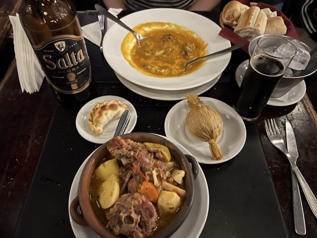 A bowl of meat, a bowl of soup, an empanada, and a tamal on a table