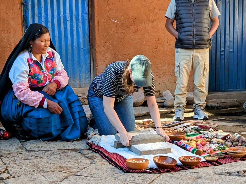 Someone grinding a flour next to a women in colorful clothing while on the Lake Titicaca homestay tour