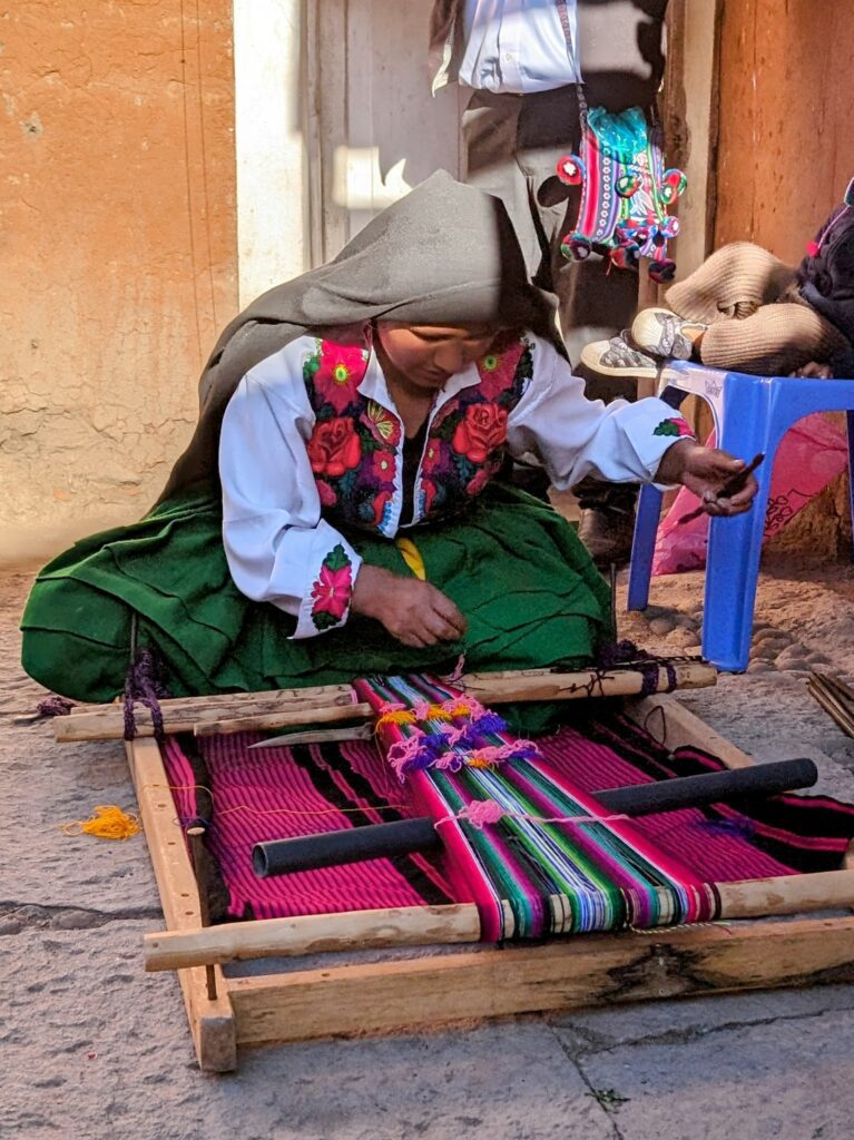 A women in colorful clothing weaving a colorful fabric as seen during the Lake Titicaca homestay tour