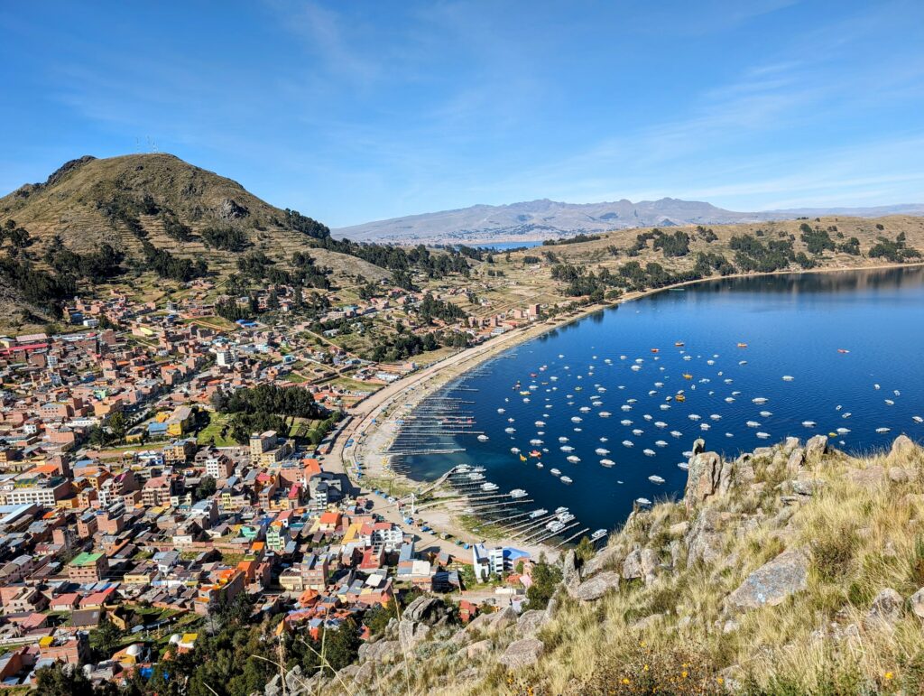 The view from the top of a mountain of a town, beach, and dock on Lake Titicaca