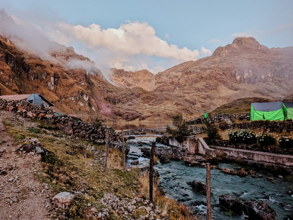 A river flowing between mountains with tents for camping on either side during the Lares Trek
