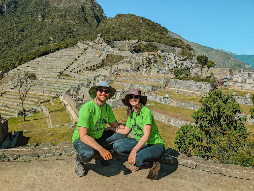 Two people squatting in front of an archaeological site in a hill