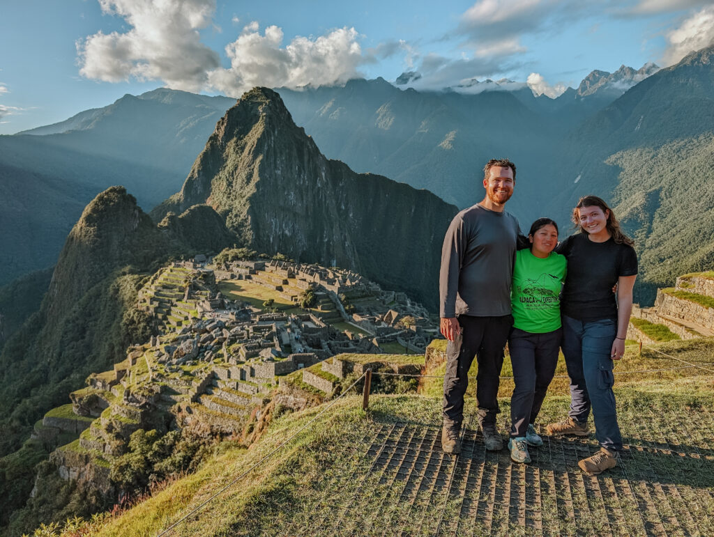 Three people standing on a platform above and in front of Machu Picchu