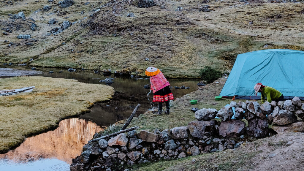 A woman throwing water into a lake in front of a green tent on the Lares Trek