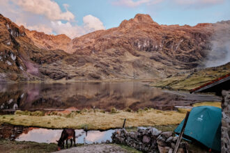 A tent in front of a lake with mountains in the background during a pink sunset on the Lares Trek