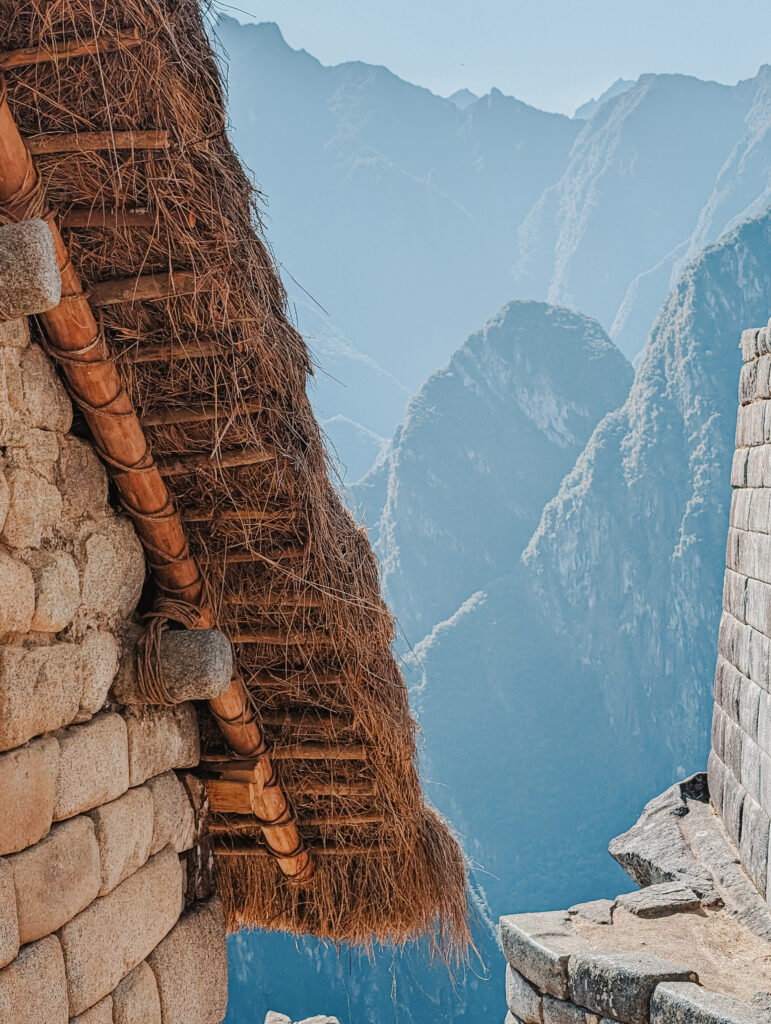 The edge of a thatched roof over a stone structure with mountains in the distance