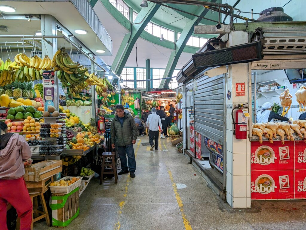 An indoor market selling chicken on one side and vegetables and fruit on the other in Lima