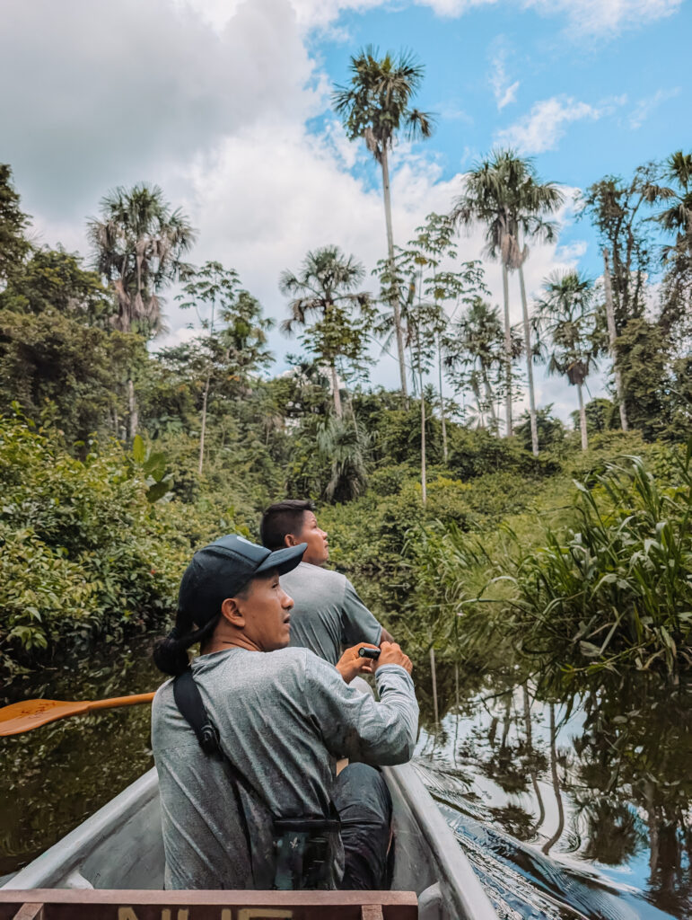 Two people looking into the rainforest while paddling a canoe when visiting the Napo Wildlife Center