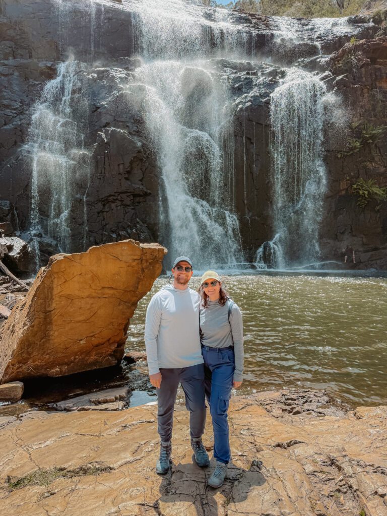 Two people standing on a large rock in front of a waterfall in the Grampians