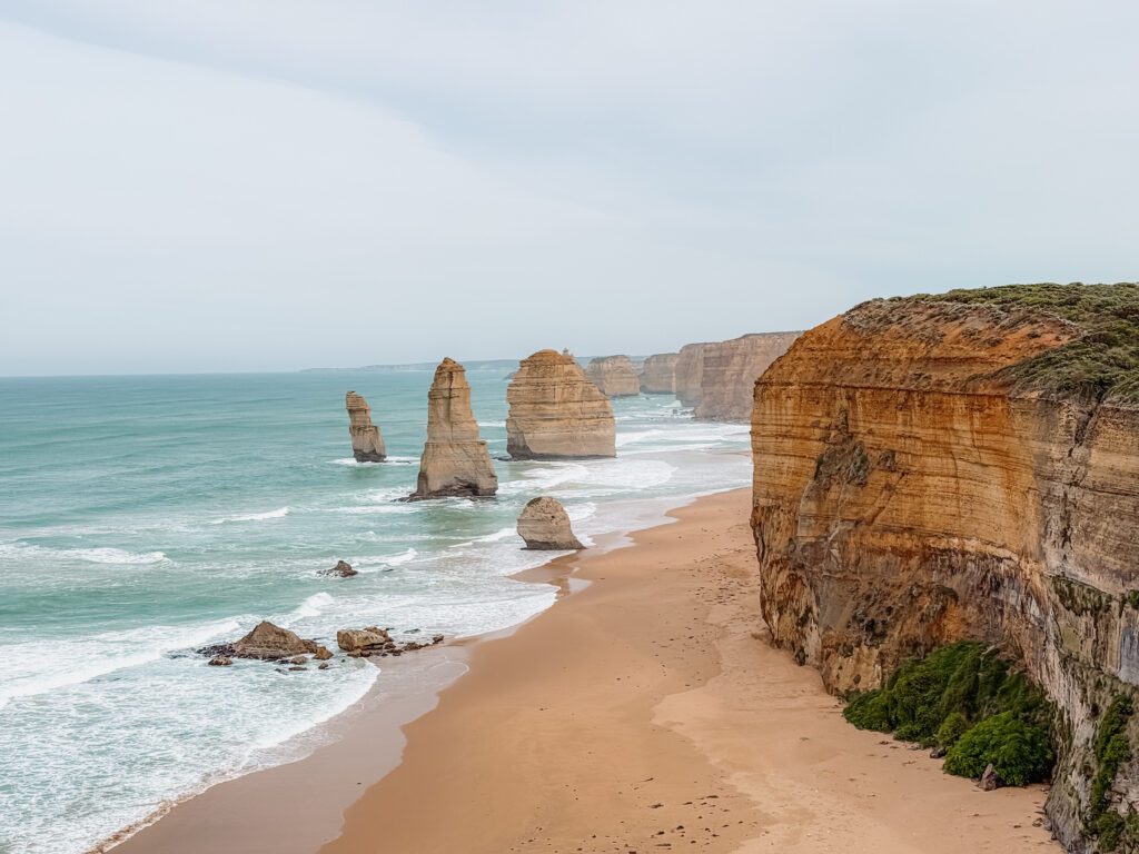 Rock formations in the ocean adjacent to a beach and cliff as seen when driving the Great Ocean Road