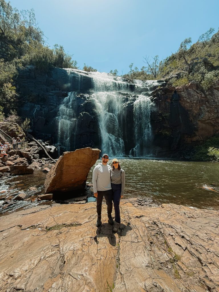 Two people standing on a large rock in front of a waterfall in the Grampians